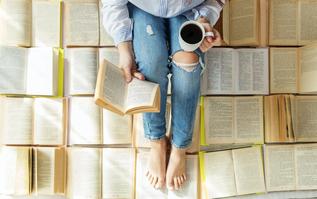 A young woman reads a book and drinks coffee. A lot of books. Concept for World Book Day